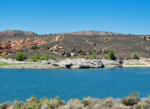 A serene lake surrounded by rocky hills and sparse greenery under a clear blue sky.